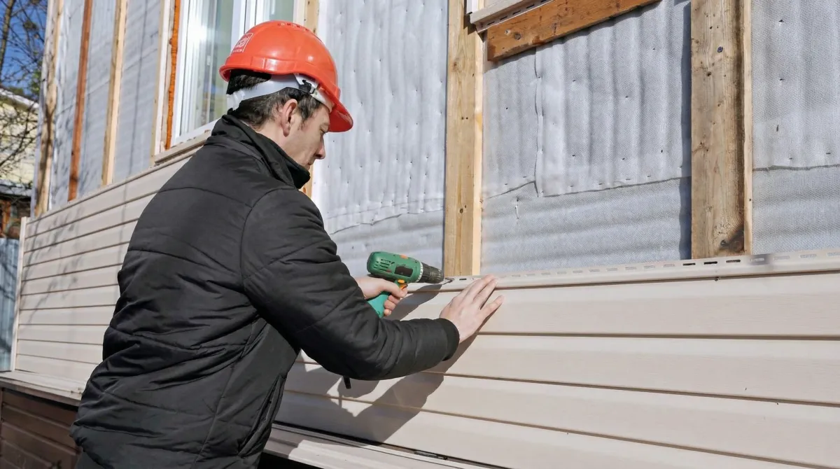 Siding replacement professional using a power drill to install new tan vinyl siding on a home exterior in Eugene, OR
